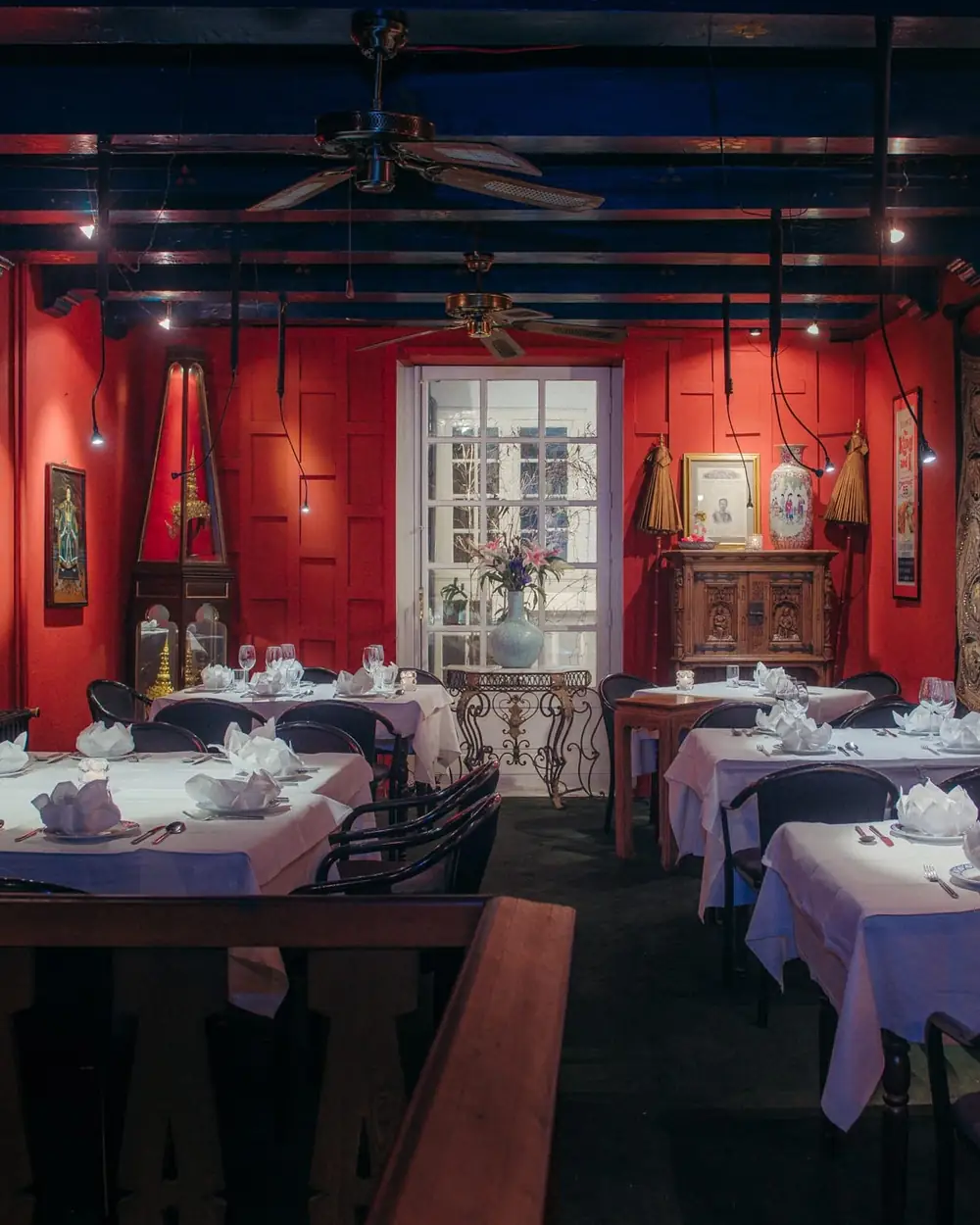 De rode zaal van het restaurant met gedekte tafels en Thaise kunst aan de muren