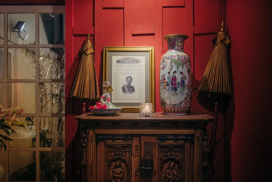 Houten kast met porselein en een ingelijste foto tegen een rode muur